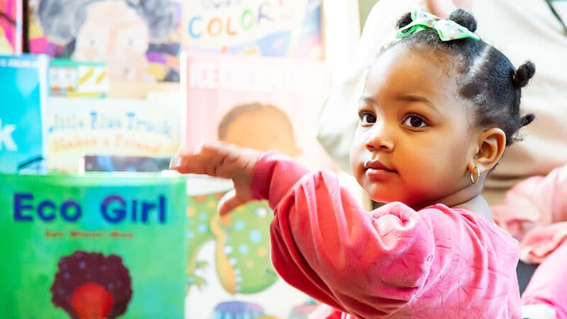 Young child using bookshelf to hold themself up to stand