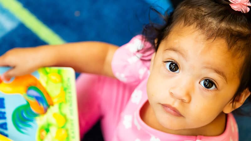Little girl holding a book and looking up at the camera