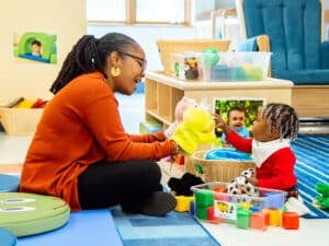 Teacher using puppet to play with infant on floor