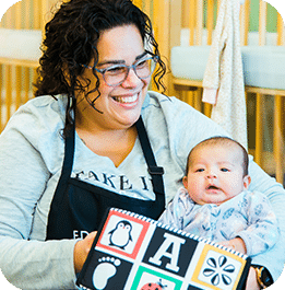 Educare West DuPage teacher holding infant and showing them a soft-touch, high-contrast book